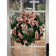 a christmas wreath hanging on the front door with red and white ribbons tied around it