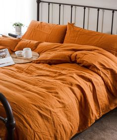 a bed with an orange comforter and two cups on the end table next to it