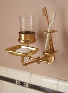 two toothbrushes and a cup on a gold plated wall mounted soap dispenser