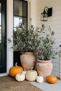 two large planters sitting on top of a door mat next to pumpkins and plants