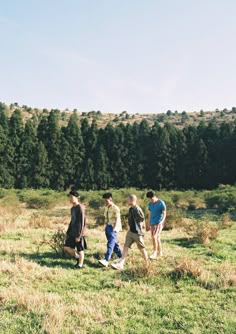 four people walking in a field with trees in the background