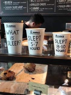 coffee cups with signs on them are sitting in front of a display case at a bakery