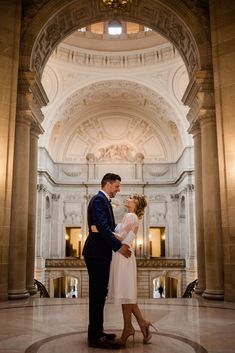 a bride and groom standing in the middle of an ornate building with columns on either side