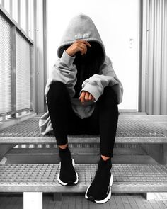 a person in a hoodie sitting on a bench with their hands behind their head