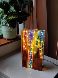 a wooden block with lights on it sitting next to a potted plant and window