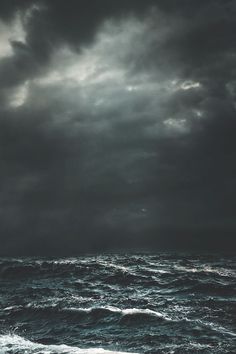 the ocean is very dark and stormy with some clouds in the sky above it,