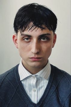 a man with black hair wearing a sweater and tie