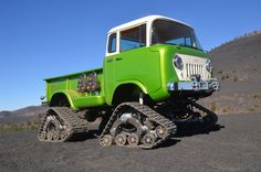 a green truck with two large wheels on it's front tire, parked in the desert