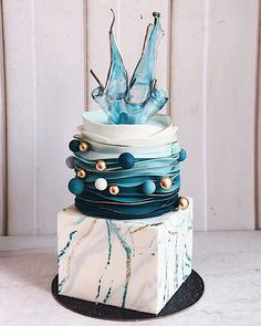 a multi layer cake with blue frosting and gold beads on the top, sitting on a marble block