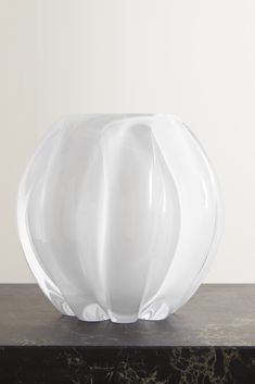 a large white vase sitting on top of a black marble table next to a wall