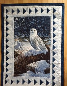 an owl sitting on top of a snow covered ground next to a patchwork wall hanging