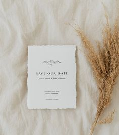 a wedding save - the - date card and some dried grass on a white sheet