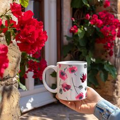 a hand holding a coffee mug with red flowers in the background