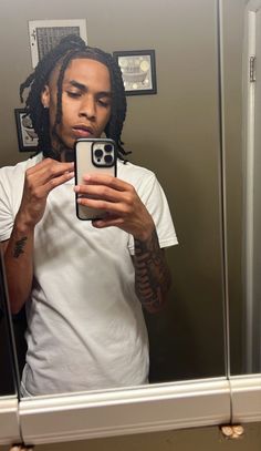 a man with dreadlocks taking a selfie in front of a bathroom mirror