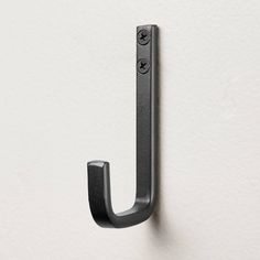 an iron hook on a white wall next to a black door handle with three holes