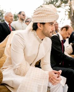 a man in a white suit and hat sitting on a couch next to other men