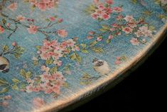 a wooden table with flowers and birds painted on the top, sitting in front of a black background