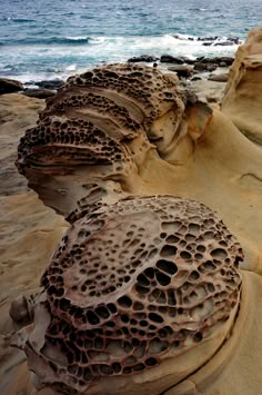 some rocks and sand on the beach by the ocean with waves coming in from the water