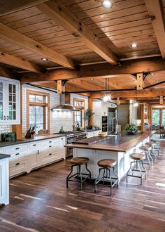 a large kitchen with wooden floors and white cabinets, an island countertop and bar stools