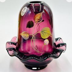 a pink glass vase sitting on top of a black stand with flowers painted on it