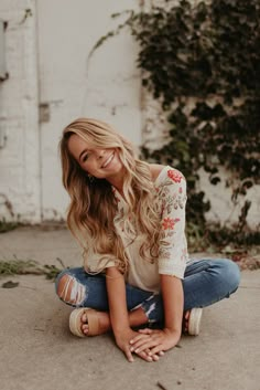 a woman sitting on the ground with her hands in her pockets and looking at the camera