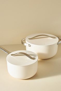 two white pots and pans with silver handles on a beige tableclothed surface