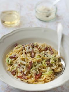 a white bowl filled with pasta covered in bacon and other toppings on top of a table