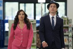 the man and woman are dressed in business attire, one is wearing a pink suit