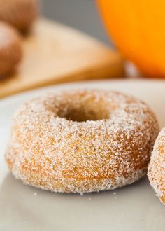 two sugared donuts sitting on top of a white plate next to an orange