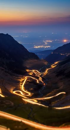 an aerial view of a winding road in the mountains at night with lights on it