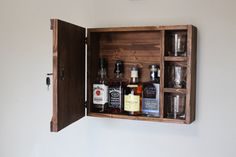 an open wooden cabinet with liquor bottles and shot glasses