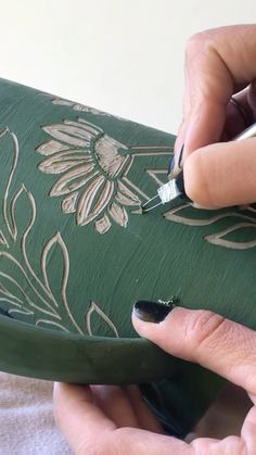 someone using a brush to paint the bottom of a green vase with flowers on it