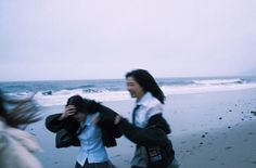 two people walking on the beach in front of the ocean