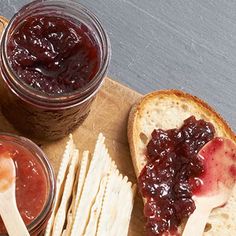 two jars of jelly and crackers on a cutting board next to some bread sticks