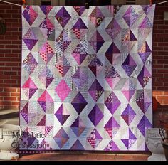 a purple and white quilt hanging on a brick wall