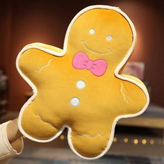 a hand holding up a yellow ginger shaped pillow with a pink bow tie on it