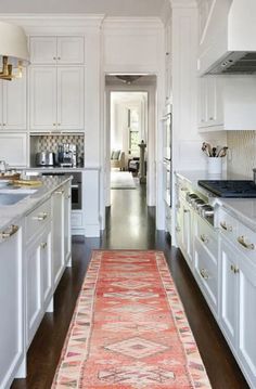 a long narrow kitchen with white cabinets and an orange runner rug in the middle of the room