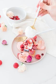 a person is spooning ice cream onto a plate with raspberries and roses