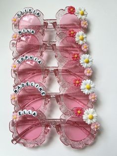 pink sunglasses with white flowers and name written on the lenses are arranged in a row