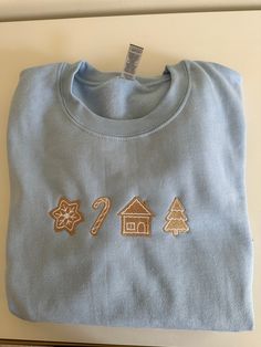 This minimalist Christmas sugar cookie crewneck is the perfect sweater to wear this holiday season. Light baby blue sweater with tan embroidered Christmas cookies. Girly Christmas embroidery, not too loud in spirit. Each Christmas cookie is shaped in holiday shaped items such as Christmas trees and candy canes. It is center chest and has white outline around the tan shapes. Unisex sizing, 50% polyester and 50% cotton. True to size, size up if you want a looser fit. Light Blue Christmas Outfit, Cookie Sweater, Butterfly Crewneck, Christmas Coal, Religious Embroidery, Embroidery Crewneck, Portrait Embroidery, Girly Christmas, Baby Blue Sweater