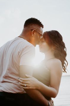 a man and woman standing next to each other in front of the ocean at sunset