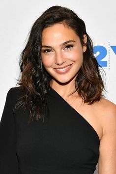 a woman in a black dress smiling at the camera with long hair and shoulder length curls