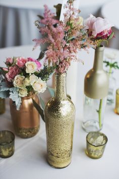 three vases with flowers in them sitting on a table next to glasses and candles