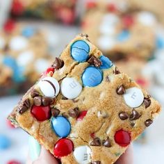 a person holding up a cookie with m & m on it's side in front of other cookies