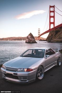 a silver car parked in front of a large body of water near the golden gate bridge