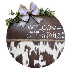 a wooden sign with a bow on it that says welcome to our home and is decorated with greenery