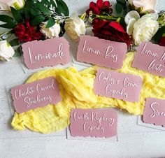 pink place cards with names on them sitting next to flowers and other items that include roses