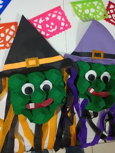 two green faces wearing witches hats on top of each other in front of colorful paper decorations