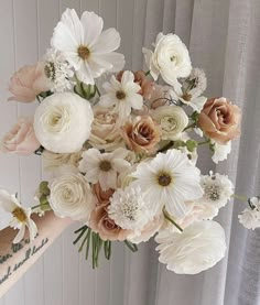 a woman holding a bouquet of white and pink flowers in front of a curtained window