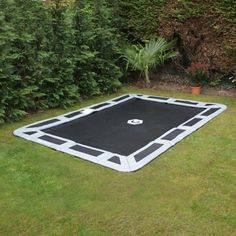 a black and white trampoline in the middle of some grass with bushes behind it